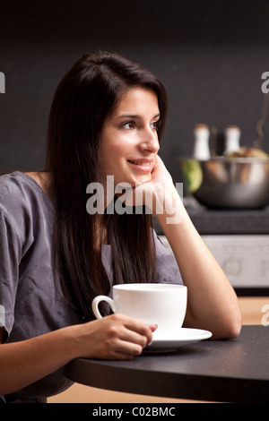 Young woman sitting in the kitchen and drinking coffee Stock Photo