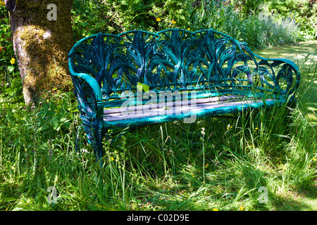 A pretty rustic wrought iron bench or seat in a shady corner of an English country garden in summer Stock Photo