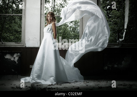 Young blonde woman in a wedding dress with fluttering veil in an urban location Stock Photo
