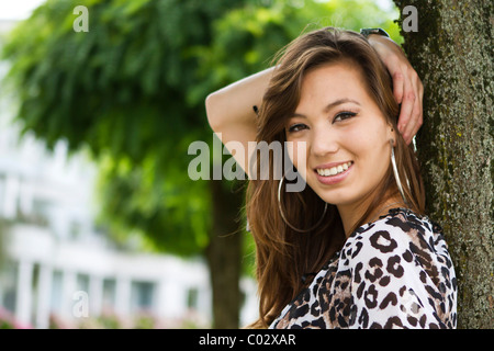 Young woman wearing leopard-print top leaning against tree Stock Photo