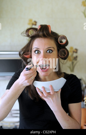 Young woman wearing rollers in hair having breakfast rushing to get to work in the morning Stock Photo