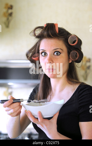 Young woman wearing rollers in hair having breakfast rushing to get to work in the morning Stock Photo