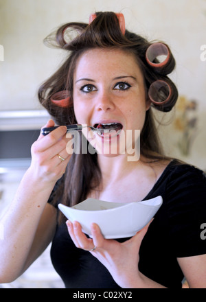 Young woman wearing rollers in hair having breakfast rushing to get to work in the morning Stock Photo