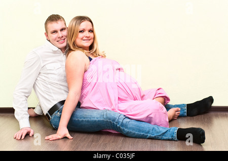Pregnant woman with her husband sitting on floor in empty room. Caucasians, a loving young couple Stock Photo
