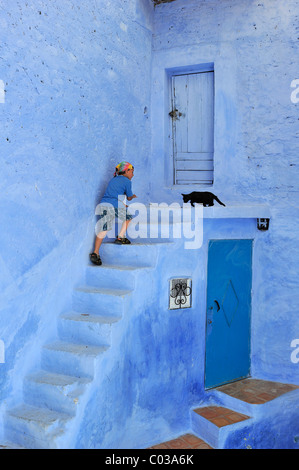 A little boy runs after a cat on a stairway, blue painted house and stairs in the medina of Chefchaouen, Morocco, Africa Stock Photo