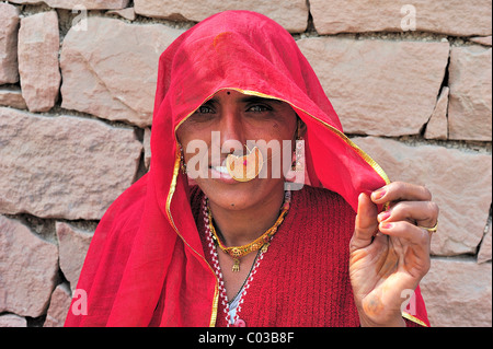 Portrait of a young Indian woman wearing a red sari and a golden nose-ring in front of a stone wall, Bishnoi ethnic group Stock Photo