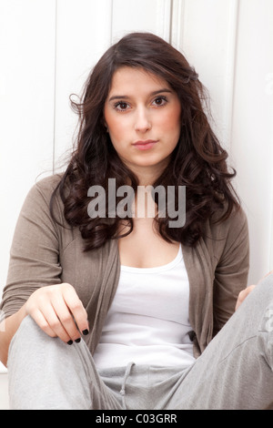 Young woman, seated and leaning against a door Stock Photo