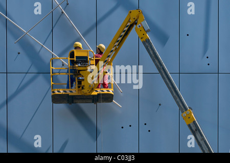 Workers wearing hard hats, standing on an articulated telescoping boom lift and working on facade elements Stock Photo