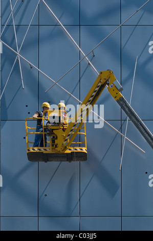 Workers wearing hard hats, standing on an articulated telescoping boom lift and working on facade elements Stock Photo