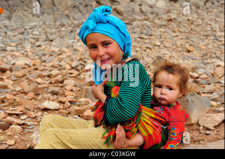 Girl wearing a headscarf carrying her little brother in a sling, High Atlas Mountains, Morocco, Africa Stock Photo