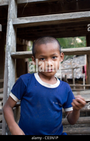 A young Burmese boy whose family fled Burma (Myanmar) is standing outside his home in Ban Tha Ta Fang, Thailand. Stock Photo