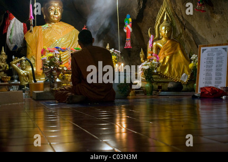 A Buddhist monk is sitting in an underground cave in front of an altar with Buddha statues at a Buddhist temple in Northern Tha Stock Photo