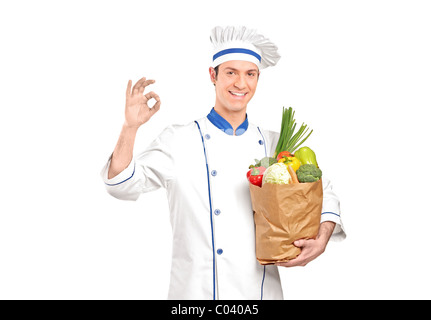 A smiling chef gesturing delicious hand sign and holding a grocery bag full with vegetables Stock Photo