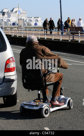 Elderly man riding an ultra light electric mobility scooter around a parked car Stock Photo