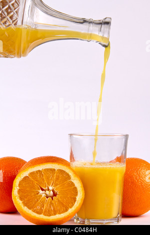 Orange juice being poured into a glass surrounded by orange fruits Stock Photo