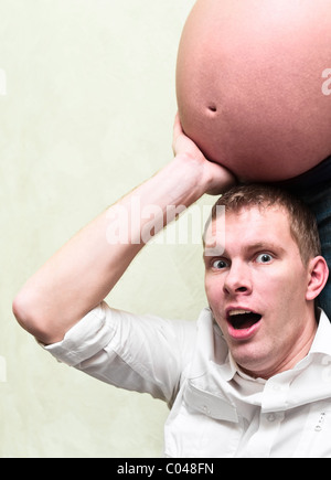 Pregnant woman with her amazed husband holding belly his hands. Caucasians, a loving young couple. Man under belly Stock Photo