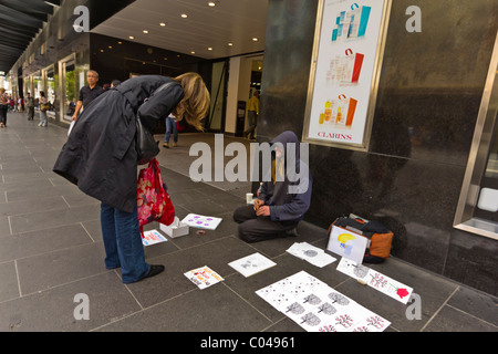 Women giving to homeless man selling art in Bourke Street Mall, Melbourne Stock Photo