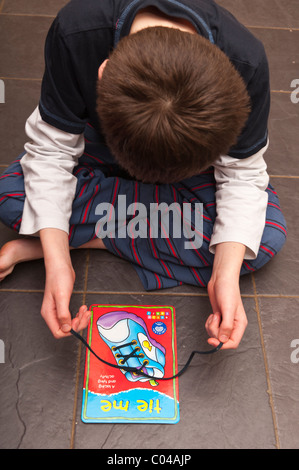 A MODEL RELEASED boy practises tying shoelaces on a learning card by orchard toys in the Uk Stock Photo