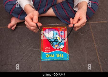 A MODEL RELEASED boy practises tying shoelaces on a learning card by orchard toys in the Uk Stock Photo