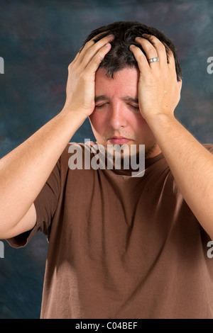 Man holds his hands to his head as he suffers from a headache caused by stress. Stock Photo