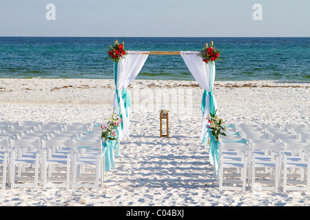 Wedding archway, chairs and flowers are arranged on the sand in preparation for a beach wedding ceremony. Stock Photo