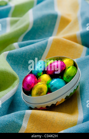 Mini chocolate easter eggs in cardboard egg box on textured wrinkled yellow and blue tablecloth Stock Photo