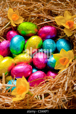 group of foil wrapped small chocolate easter eggs in various colors sitting in a hay birds nest on an oak table Stock Photo