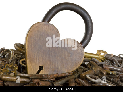 A brass tinted heart lock rests on a pile of old keys. Finding the right key to open a heart lock.  Isolated. Stock Photo