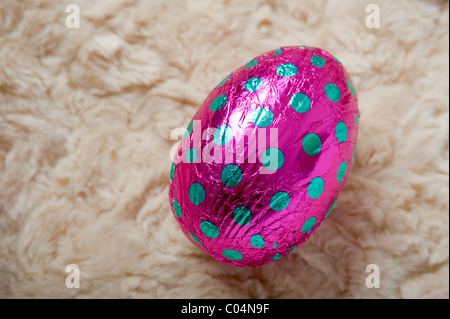 Single large chocolate easter egg wrapped in pink with turquoise spots foil at an angle on a cream wool fleece background Stock Photo