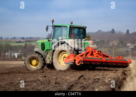 Tractor harrowing field after plowing in preparation for spring sowing. Stock Photo