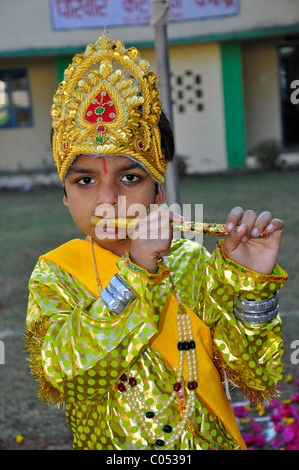 A boy posing as Lord Krishna wearing colorful dress and playing a flute Stock Photo