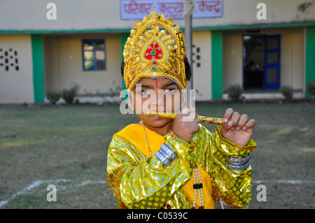 A boy posing as Lord Krishna wearing colorful dress and playing a flute Stock Photo