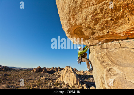 Male rock climber struggles for his next grip as he clings to a sheer cliff. Stock Photo