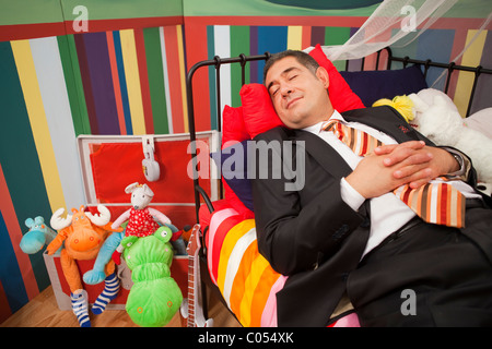 Mature man wearing full suit sleeping happly in children's bed - Relaxation - Humour - Childish Stock Photo