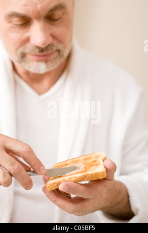 Senior mature man having breakfast butter toast wear bathrobe Stock Photo