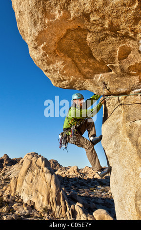 Male rock climber struggles for his next grip as he clings to a sheer cliff. Stock Photo