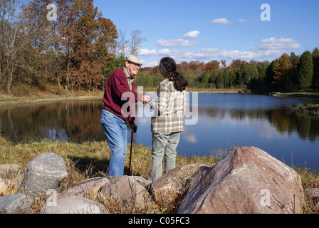 Woman giving helping hand to Senior man by a lake. Stock Photo