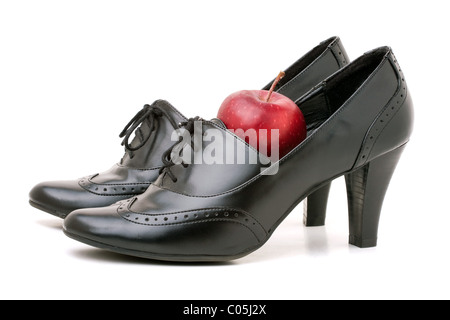 A pair of black leather high heel shoes with a red apple sitting in one of them - great image for a teaching or education theme. Stock Photo