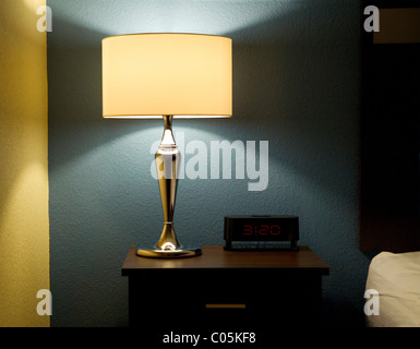 Lamp, digital clock, and end table next to a bed. Stock Photo