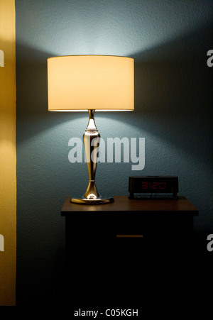 Lamp, digital clock, and end table next to a bed. Stock Photo