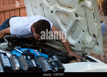Man working on car in yard. Do it yourself mechanic performing auto repair. Examining engine compartment for signs of trouble. Stock Photo