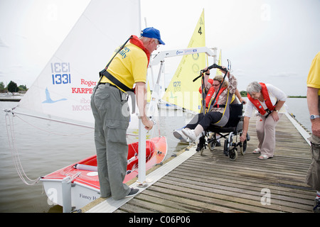 Sailing instructor with the Waveney Sailability Trust helps disabled woman into sailing dinghy using an Oxford Dipper Stock Photo