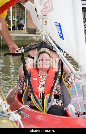 Sailing instructor with the Waveney Sailability Trust helps disabled woman into sailing dinghy using an Oxford Dipper Stock Photo