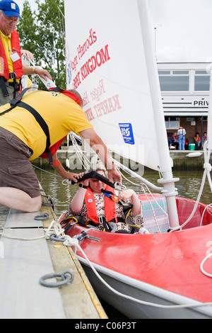 Sailing instructor with the Waveney Sailability Trust helps disabled woman into sailing dinghy Stock Photo