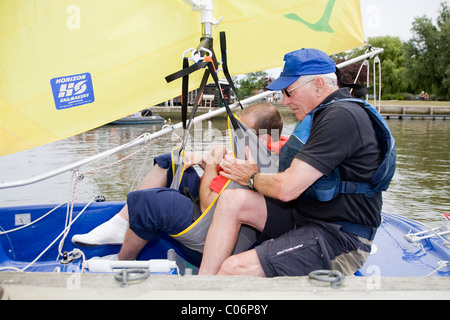Disabled man is helped into sailing dinghy by his instructor with the aid of a pool hoist Stock Photo