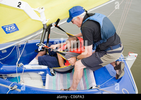 Sailing instructor with the Waveney Sailability Trust helps disabled man into sailing dinghy Stock Photo