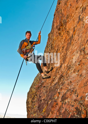 Climber rappels from the summit of a rock spire after a successful ascent. Stock Photo