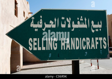 A sign points towards a handicrafts store in Oman. The bilingual sign is written in Arabic and English. Stock Photo