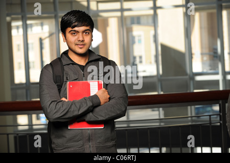 Portrait of young Indian student with school backpack holding notebook inside school building Stock Photo