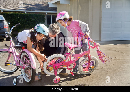 Dad and big sister adjust the training wheels of his five year old daughter's bicycle as she learns to ride in California. Stock Photo